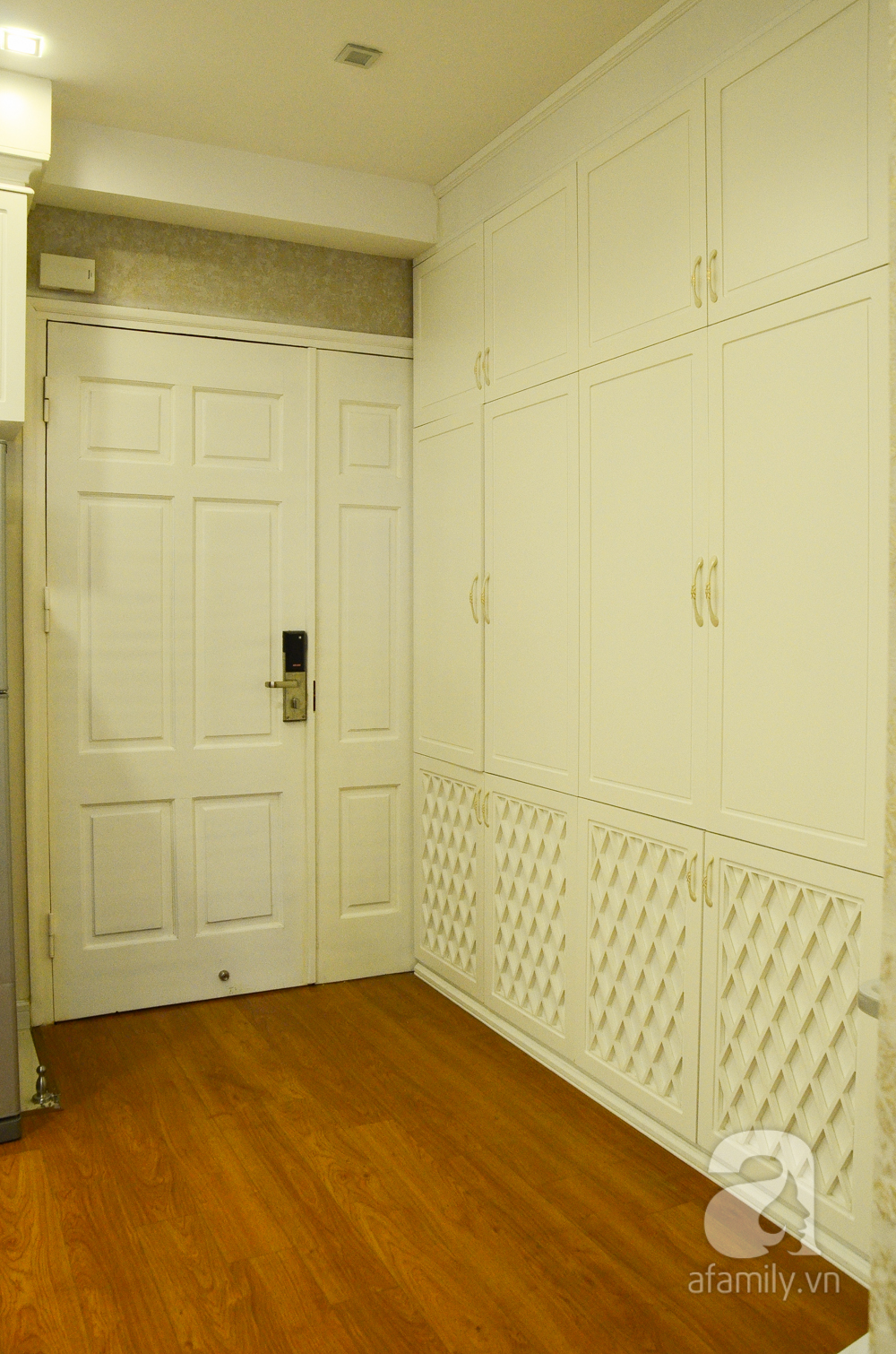 Cửa chính vào căn hộ khá rộng cùng tone màu với tủ giày trắng lớn cao sát trần, thiết kế hiện đại